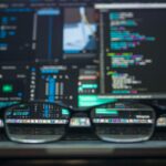 a pair of black glasses sitting on a laptop keyboard with numerous digitized windows open on the screen