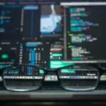 a pair of black glasses sitting on a laptop keyboard with numerous digitized windows open on the screen